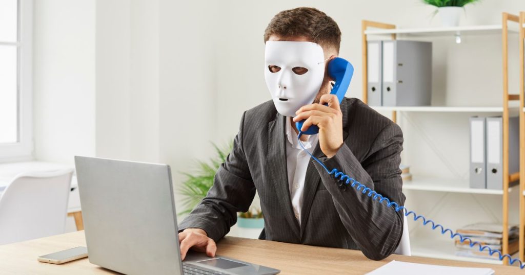 Man with white mask, talking on the phone while working on the laptop