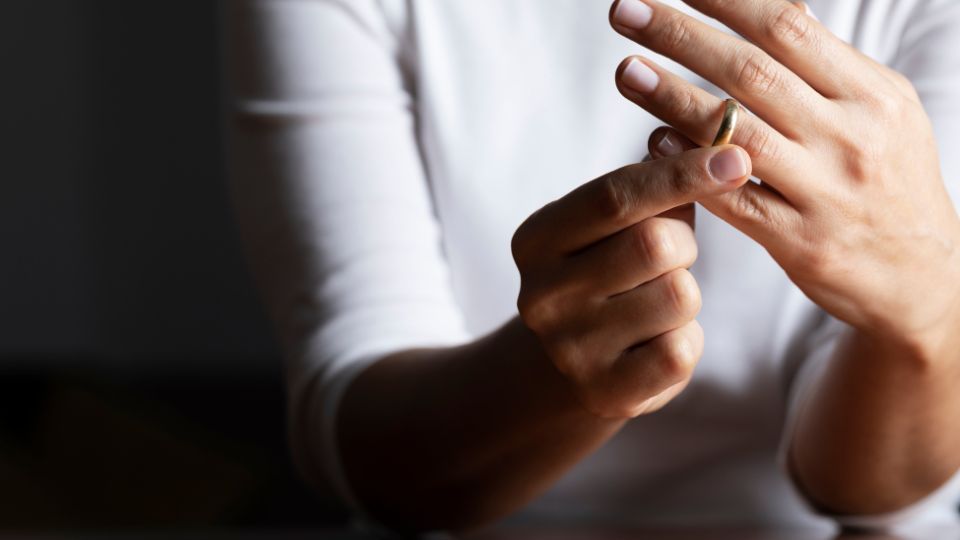 A person in a white shirt is removing a wedding ring from their ring finger, indicating a moment of personal decision or change in marital status.