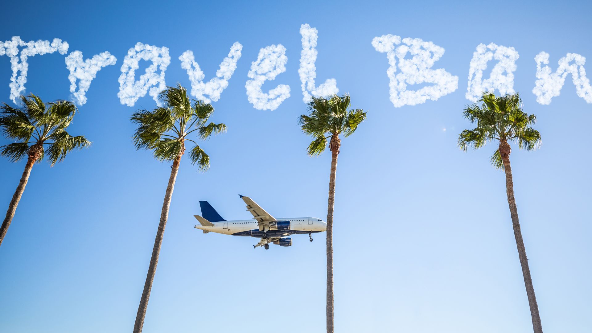 A commercial airplane flying low over four palm trees, with the words 'Travel Ban' written in the sky with cloud-like letters against a clear blue background.