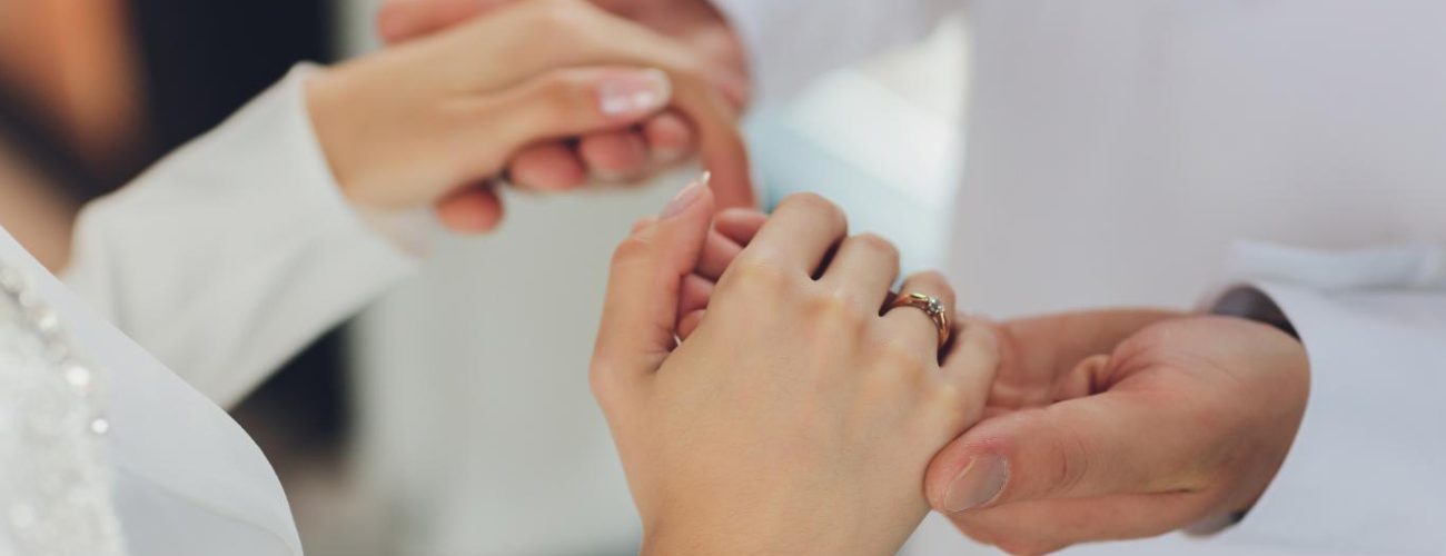 A close-up photograph of a bride and groom's hands as they exchange wedding rings, a symbolic gesture capturing the essence of matrimonial vows and the beginning of their lifelong journey together.