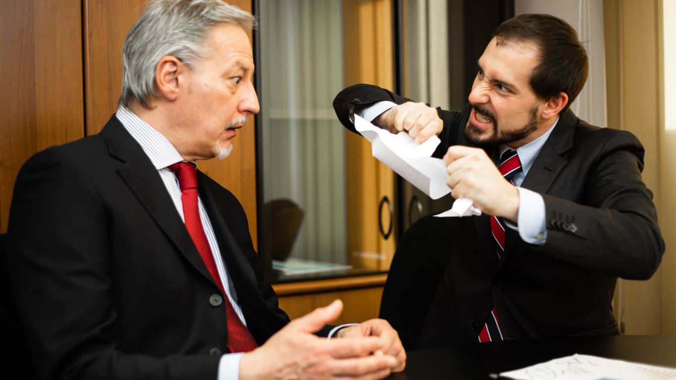 A businessman angrily tearing a contract in half in front of another individual. The shocked expression of the other person signifies a heated argument over a breach of contract.