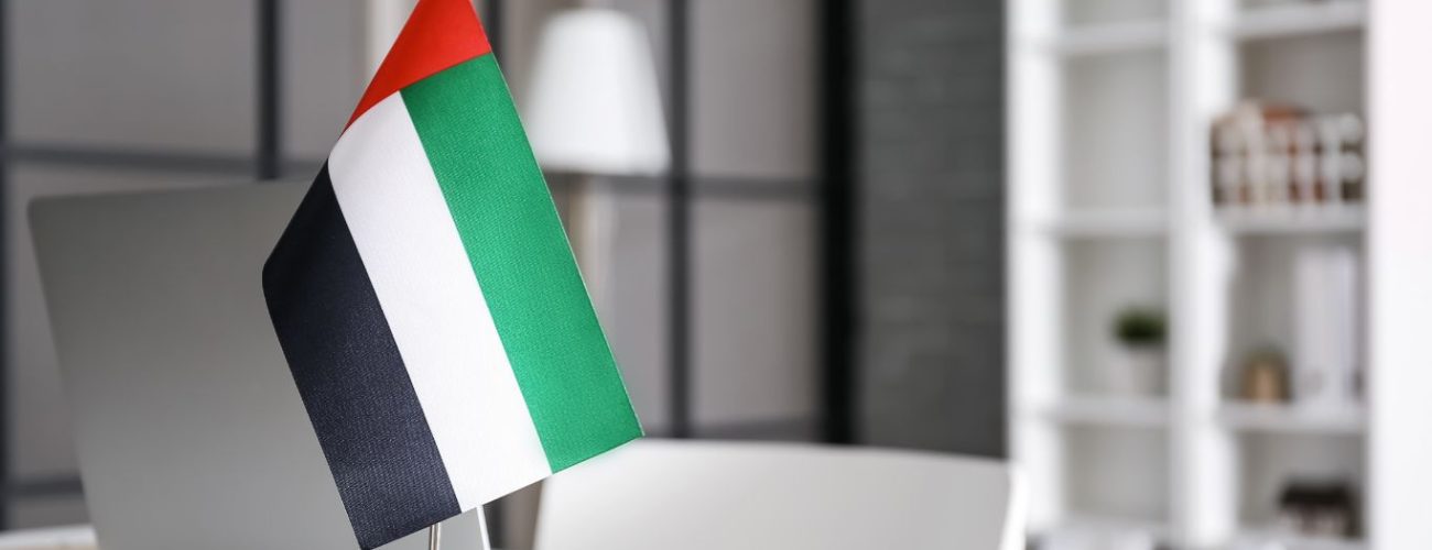 A UAE flag displayed on a small stand beside a laptop in a modern, minimalist office setting, representing national pride or business operations within the UAE, possibly related to UAE visa amnesty.